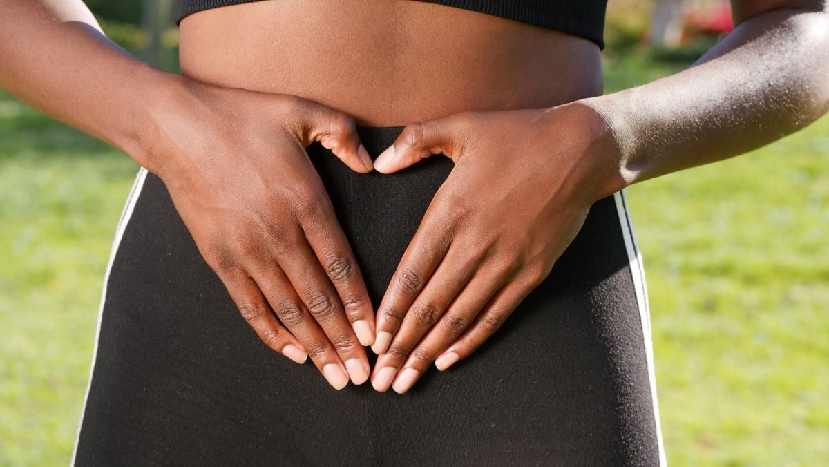 Mujer al aire libre formando un corazón con las manos sobre su abdomen, símbolo de bienestar digestivo