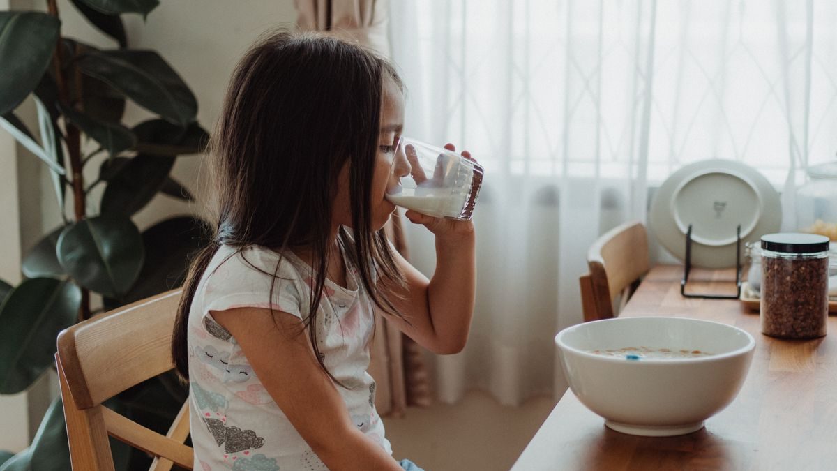 Niña tomando un vaso de leche en el desayuno